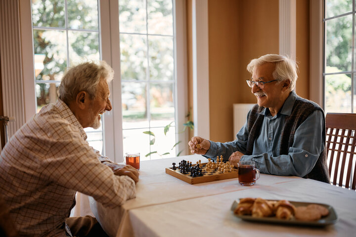 Happy senior men talk while playing chess at nursing home.