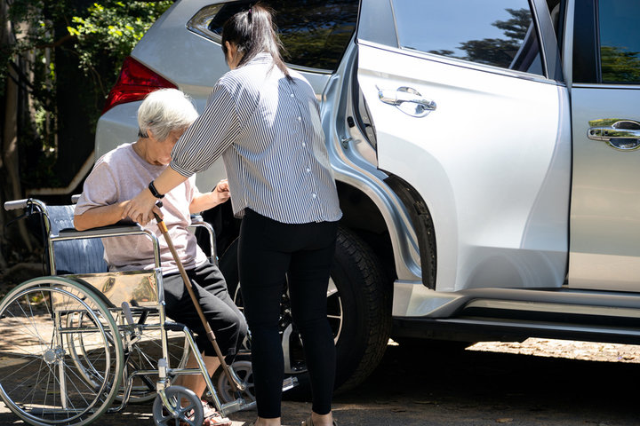 resident getting out of a wheelchair and carer helping her into a car