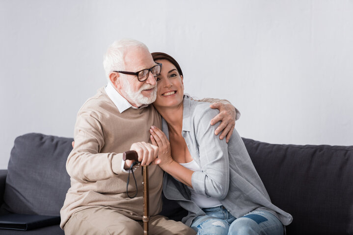 father and adult daughter smiling on sofa together 